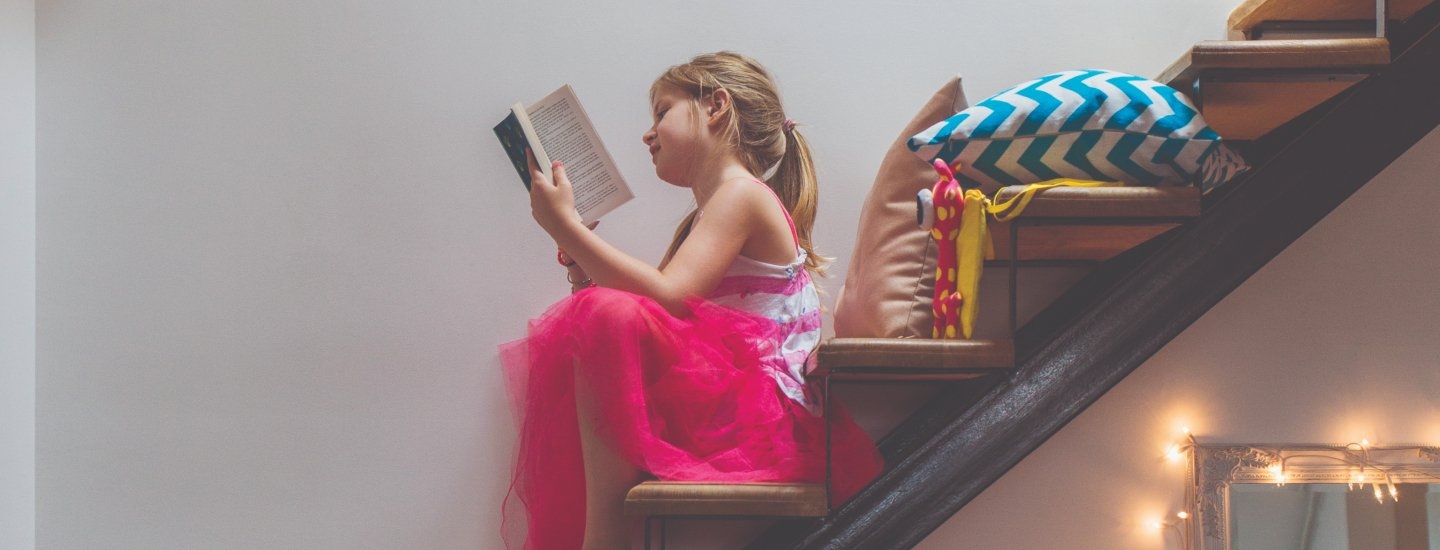 A young girl sitting reading a paperback book on some stairs